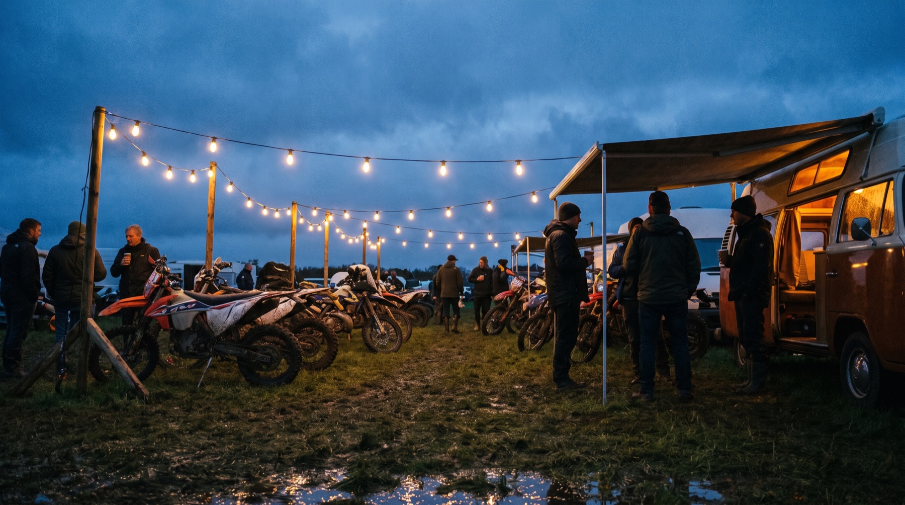 Festival paddock at dusk under festoon lights with rows of dirt bikes