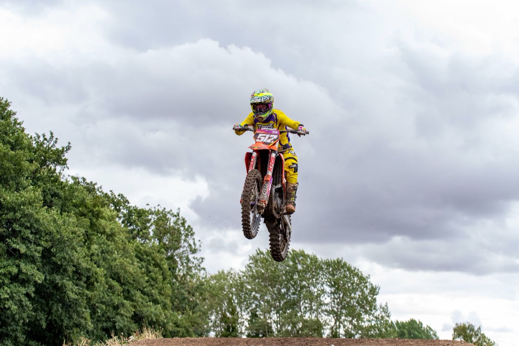 Motocross rider in yellow kit in the air over a jump against a cloudy sky