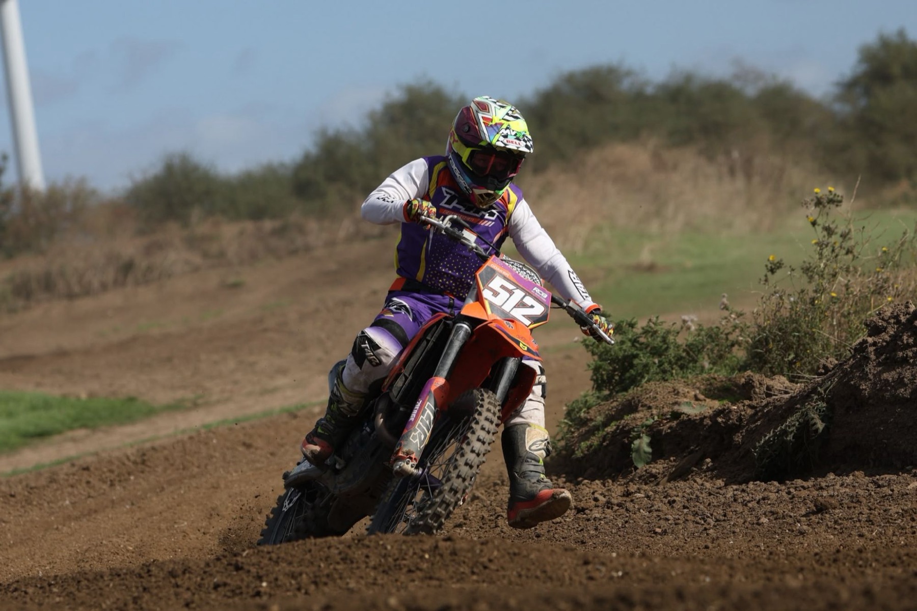 Motocross rider in purple kit leaning an orange bike through a dirt corner